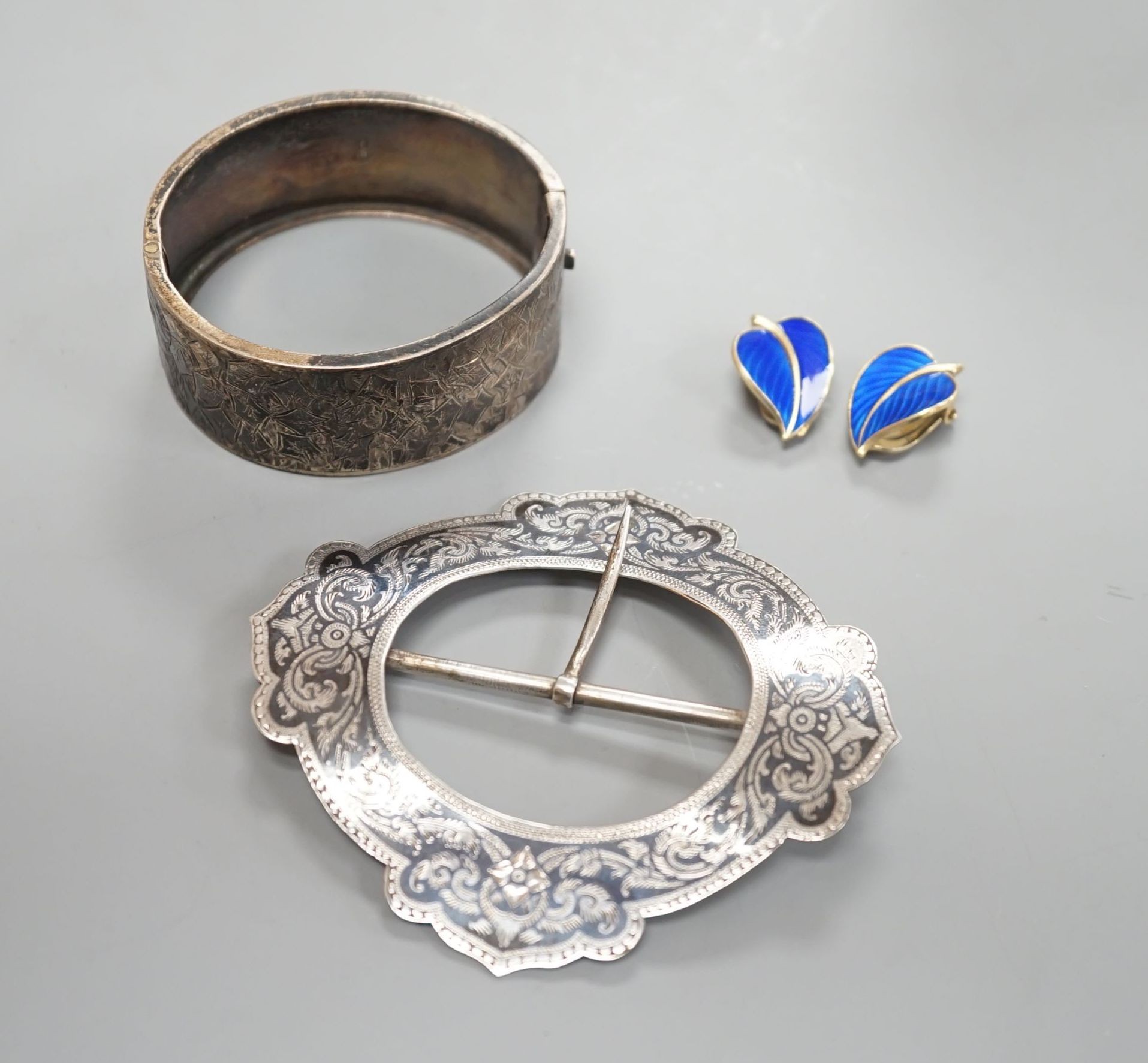 A late Victorian engraved silver hinged bangle, a white metal and niello buckle and a pair of mid 20th century Norwegian gilt 925 and enamel leaf ear clips by Hans Myhre.